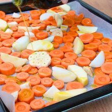 Morcovi, măr și ceapă stropite cu ulei de măsline pe tavă, pregătite pentru copt la supa cremă cu ghimbir