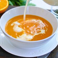 Supă cremă de morcovi copți cu ghimbir și măr, servită în bol cu smântână turnată deasupra