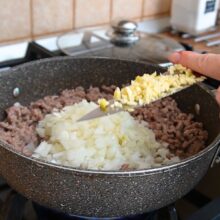 Ceapă și usturoi tocate adăugate peste carne tocată în tigaie, pentru baza sosului de lasagna