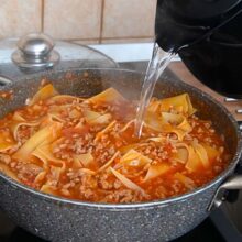 Adăugarea apei fierbinți în sosul de lasagna la tigaie pentru a permite gătirea corectă a foilor
