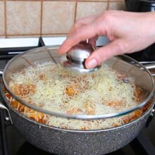 Cașcaval ras presărat peste lasagna la tigaie și acoperit cu capac pentru topire