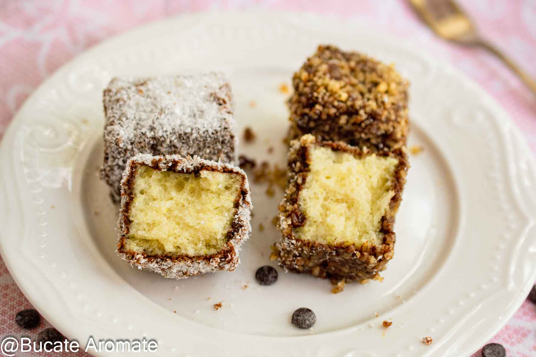 Două bucăți tăiate de lamington vegan, cu blat aerat, strat subțire de ciocolată și înveliș de nucă de cocos sau nucă măcinată.