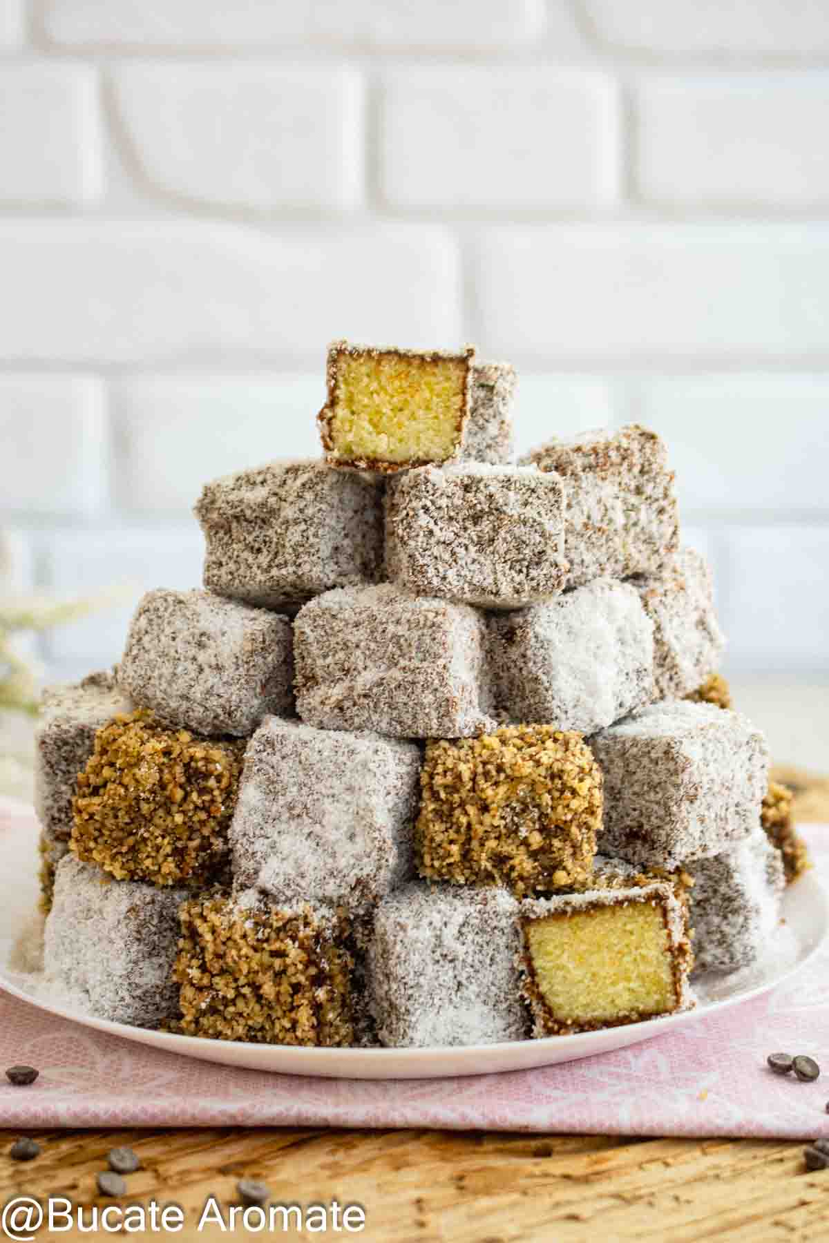 Prăjituri tăvălite vegane stivuite pe platou, cu glazură de ciocolată, cocos și bucăți tăiate care arată blatul galben și pufos.