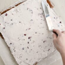 Întinderea uniformă a cremei cu vișine pe foaia de blat pentru rularea tortului.