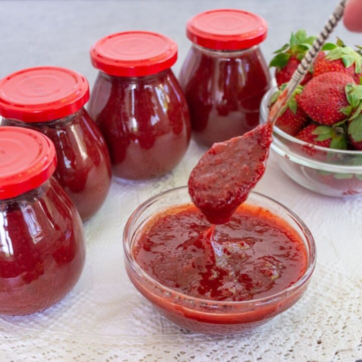 Gem de căpșuni fără conservanți, servit într-un bol, cu borcane de gem și căpșuni proaspete în fundal