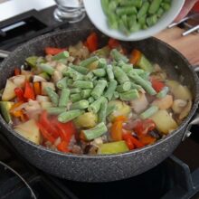 Fasolea păstăi congelată adăugată peste legumele fierte pe jumătate, în ghiveciul de legume gătit fără apă