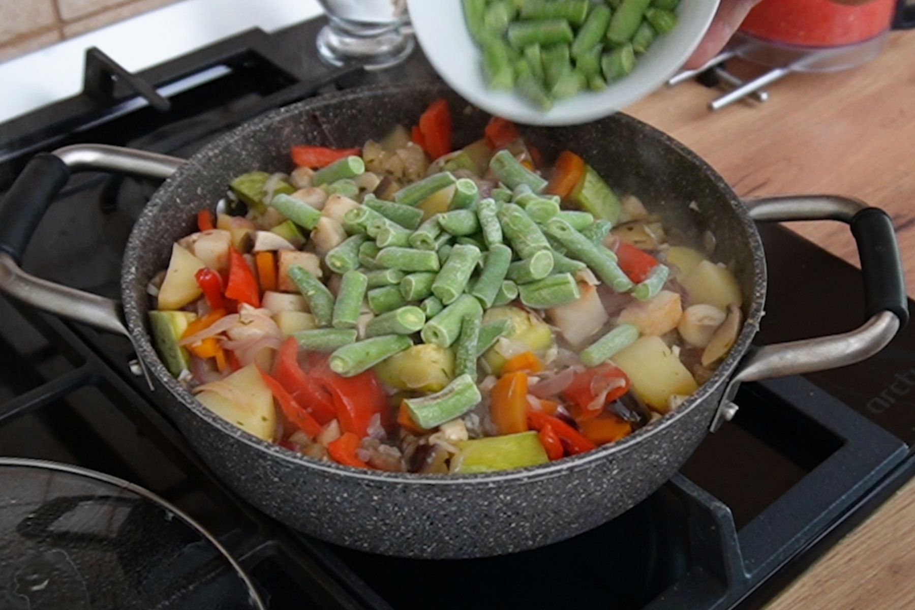 Fasolea păstăi congelată adăugată peste legumele fierte pe jumătate, în ghiveciul de legume gătit fără apă