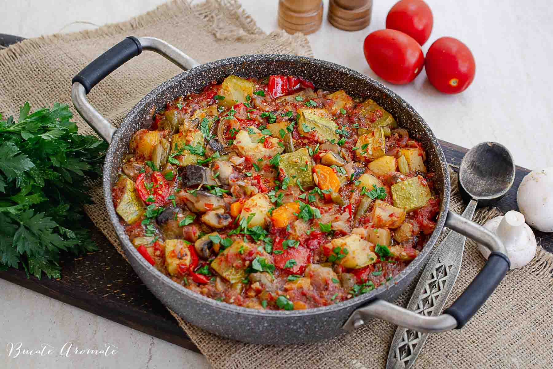 cratiță cu ghiveci de legume abia scoasa din cuptor presarat cu patrunjel verde inainte de servire