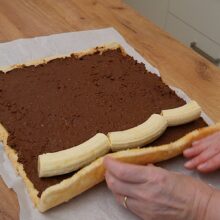 Blatul se unge cu crema ganache și se așază bananele întregi înainte de rularea finală a ruladei