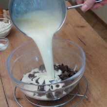 Smântâna pentru frișcă încălzită se toarnă peste ciocolată pentru a prepara ganache-ul pentru ruladă