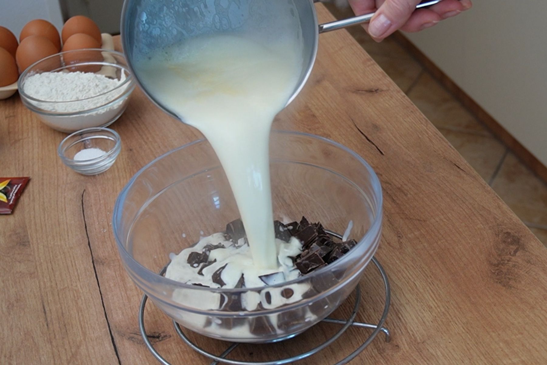 Smântâna pentru frișcă încălzită se toarnă peste ciocolată pentru a prepara ganache-ul pentru ruladă