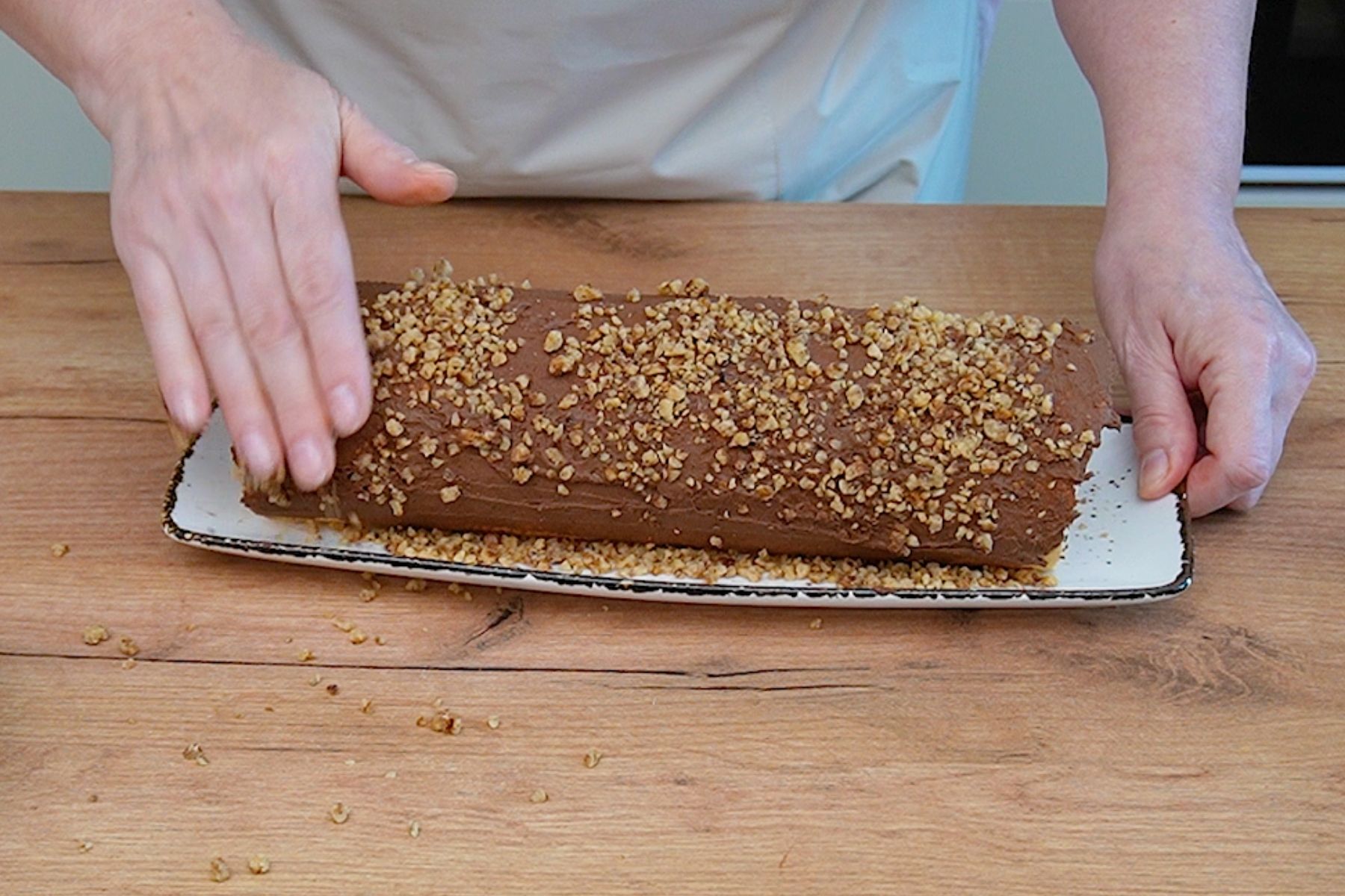 Rulada umplută și îmbrăcată în cremă de ciocolată este tapetată cu crocant de nuci pentru textură