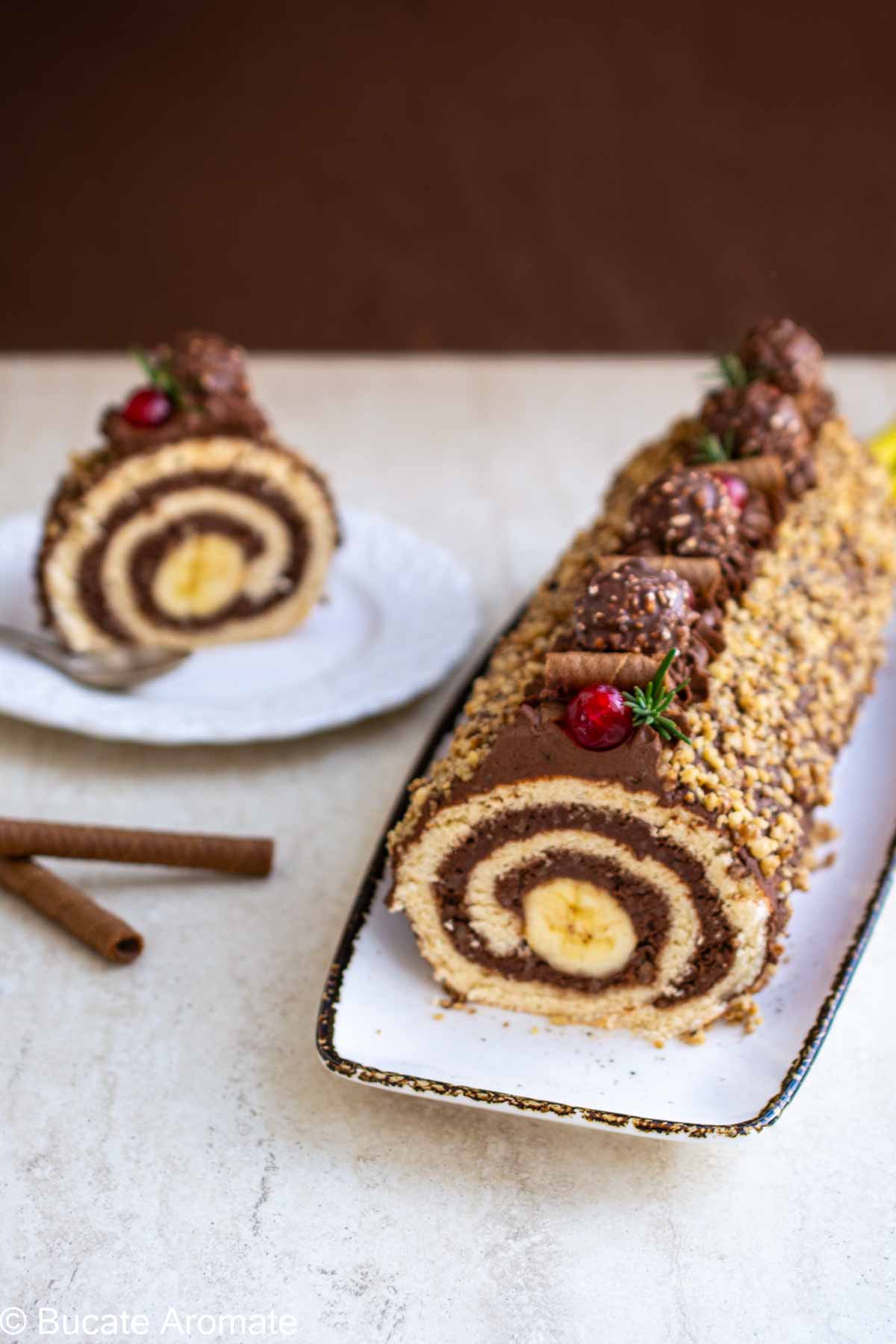 Ruladă cu ciocolată, banane și crocant de nuci, decorată cu bomboane și cireșe confiate – vedere din lateral.