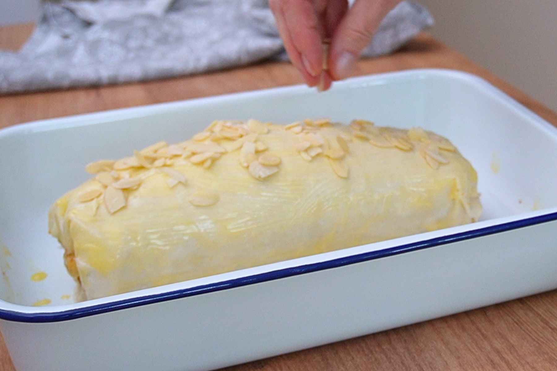 Ștrudel cu mere uns cu unt și presărat cu fulgi de migdale înainte de coacere