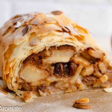 Ștrudel cu mere feliate, nucă și stafide, învelit în foi subțiri crocante, decorat cu fulgi de migdale și zahăr pudră.
