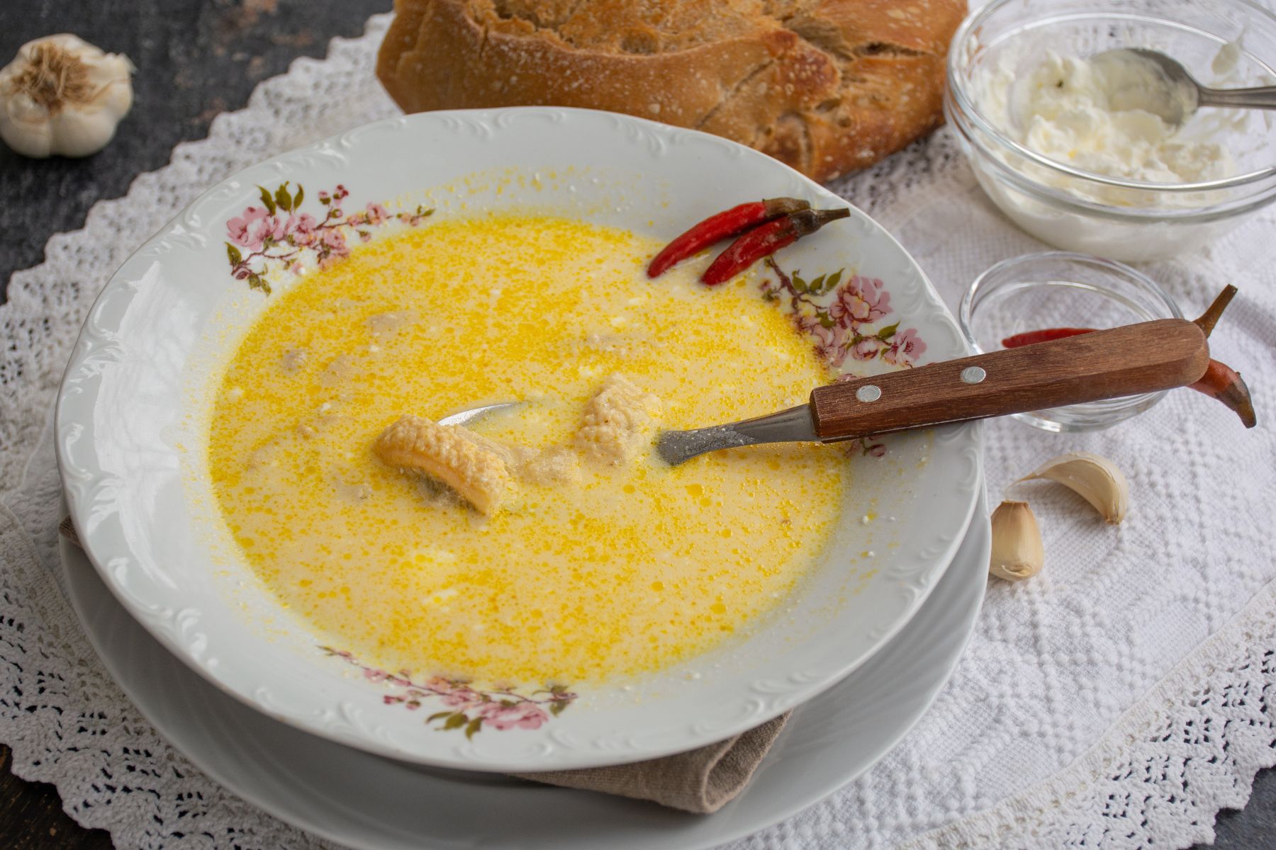 Farfurie cu ciorbă de burtă cremoasă, servită cu ardei iute, usturoi și pâine