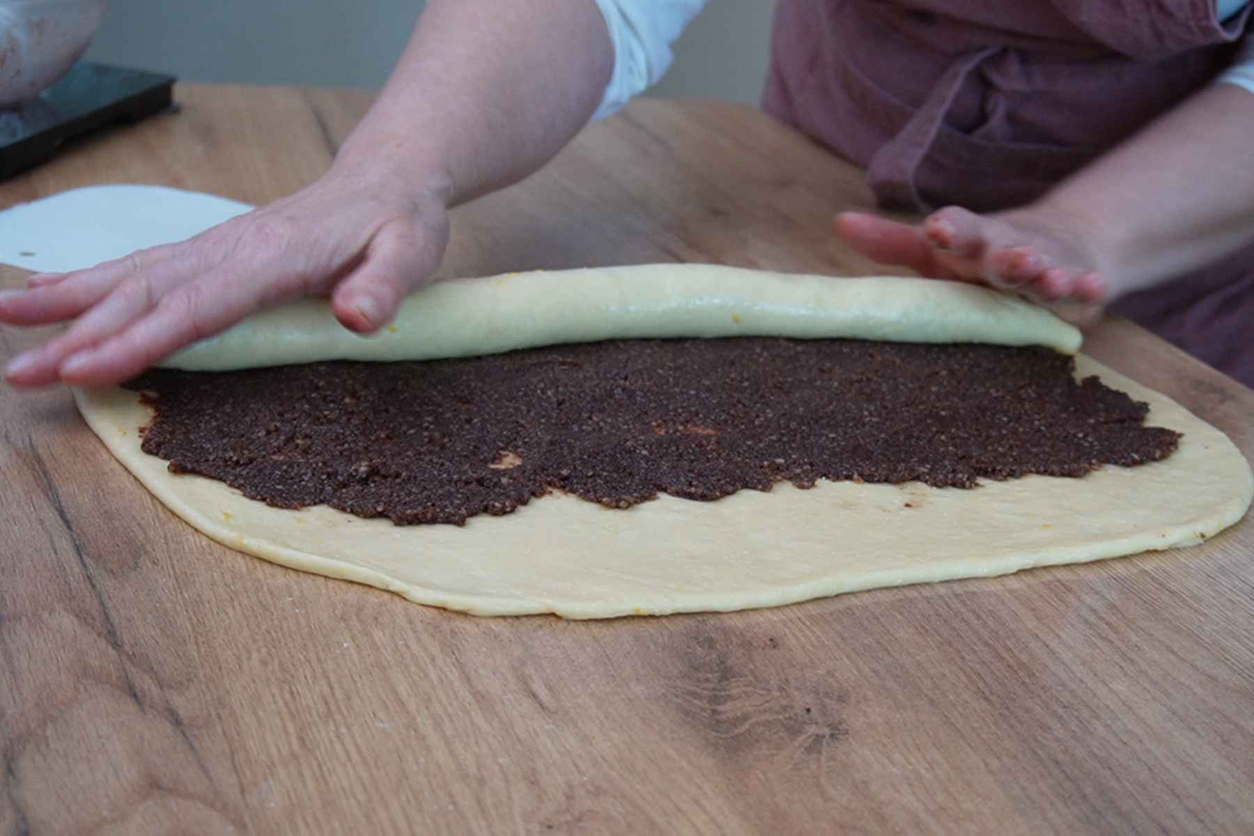 Aluat de cozonac întins cu umplutură de nucă și cacao, rulat pentru melci