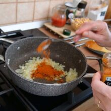 Adăugare pudră de curry peste ceapa călită la începutul rețetei de curry de năut cu lapte de cocos și unt de arahide