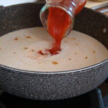 Turnare lapte de cocos și suc de roșii în tigaie pentru sosul cremos al curry-ului de năut – rețetă simplă de post