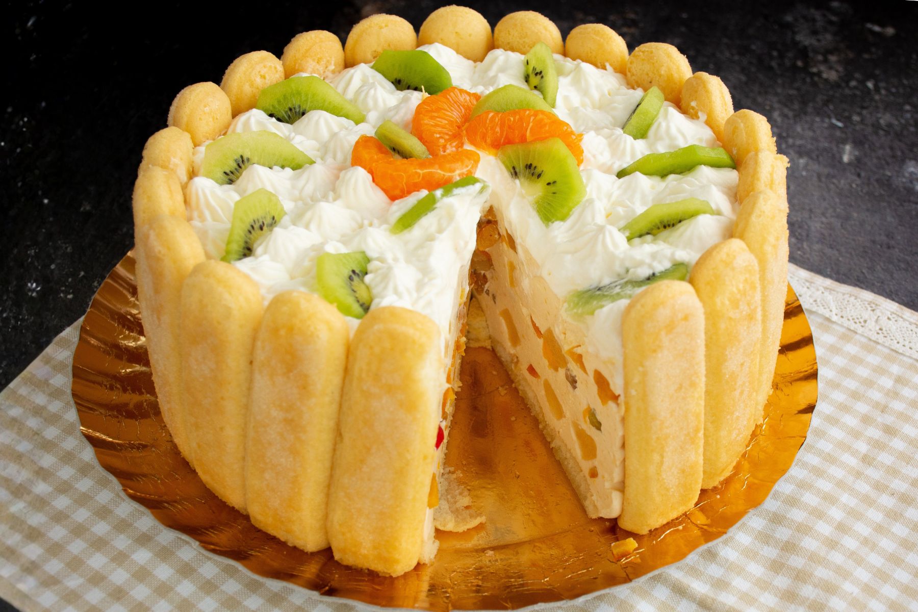Tort Diplomat cu fructe și pișcoturi, decorat cu frișcă naturală, kiwi și mandarine, cu o felie tăiată