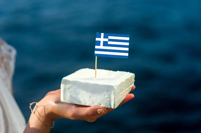 bloc de brânză feta ținut în palmă cu steagul Greciei