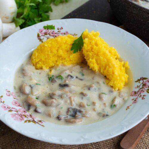 farfurie alba cu ciulama cremoasa de ciuperci servita cu mamaliguta alaturi