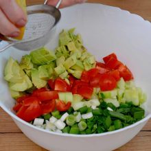 suc de lamaie turnat prin sita peste cuburile de avocado din salata