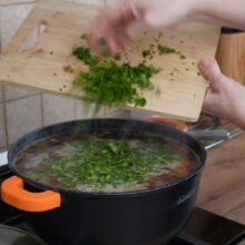 Leuștean proaspăt tocat presărat peste ciorba fierbinte, oala acoperită pentru aromatizare finală