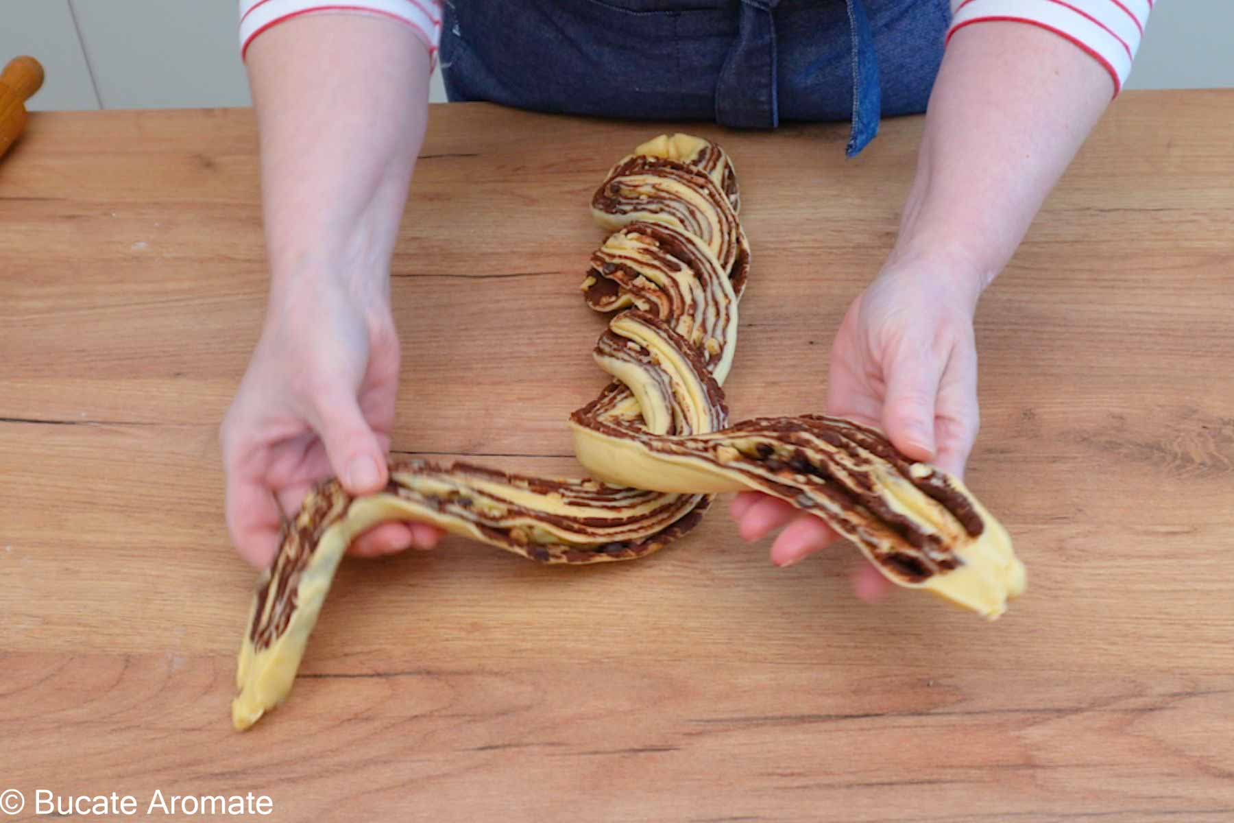 Ruloul de aluat tăiat pe lungime și împletit în două, cu umplutura de ciocolată vizibilă