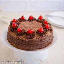 Tort de post cu ciocolată și cremă fină, decorat cu cireșe confiate și ciocolată rasă, așezat pe suport alb