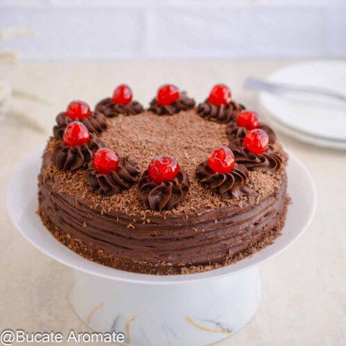 Tort de post cu ciocolată și cremă fină, decorat cu cireșe confiate și ciocolată rasă, așezat pe suport alb