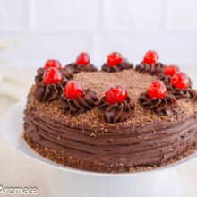 Tort de post cu ciocolată pe suport alb, decorat cu aveline de cremă, cireșe confiate și ciocolată rasă