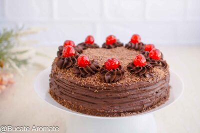 Tort de post cu ciocolată pe suport alb, decorat cu aveline de cremă, cireșe confiate și ciocolată rasă