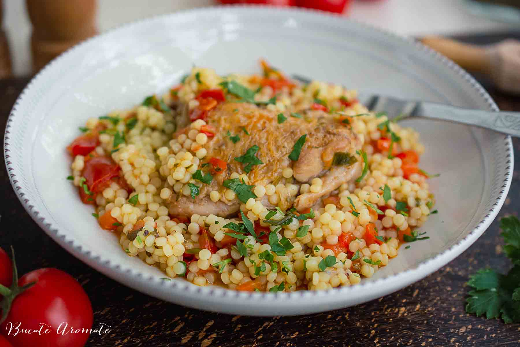 farfurie albă cu cuscus cu legume și pulpă de pui așezată pe fundal de lemn