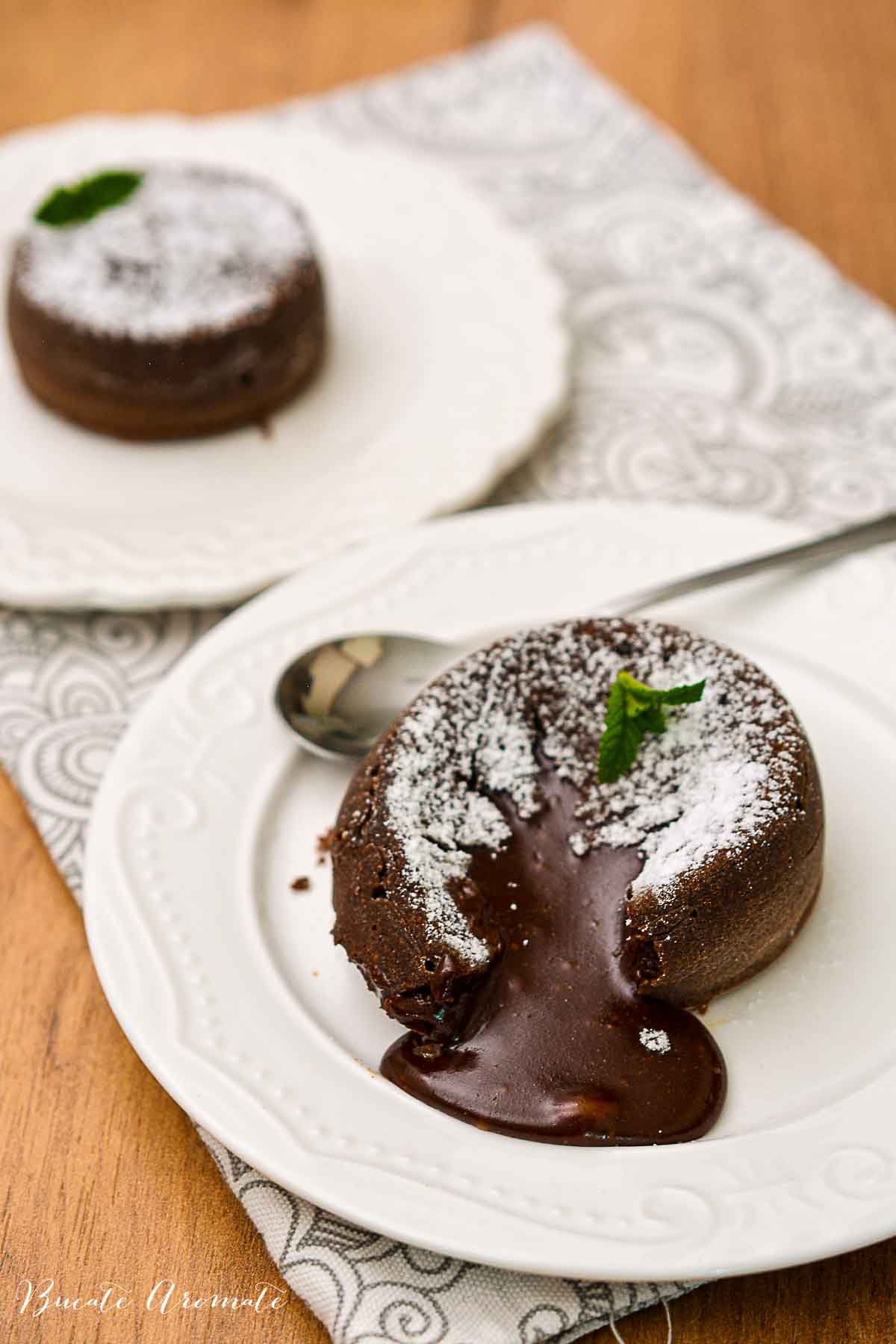 Desert lava cake cu interior fondant, prezentat elegant cu mentă proaspătă și zahăr pudră