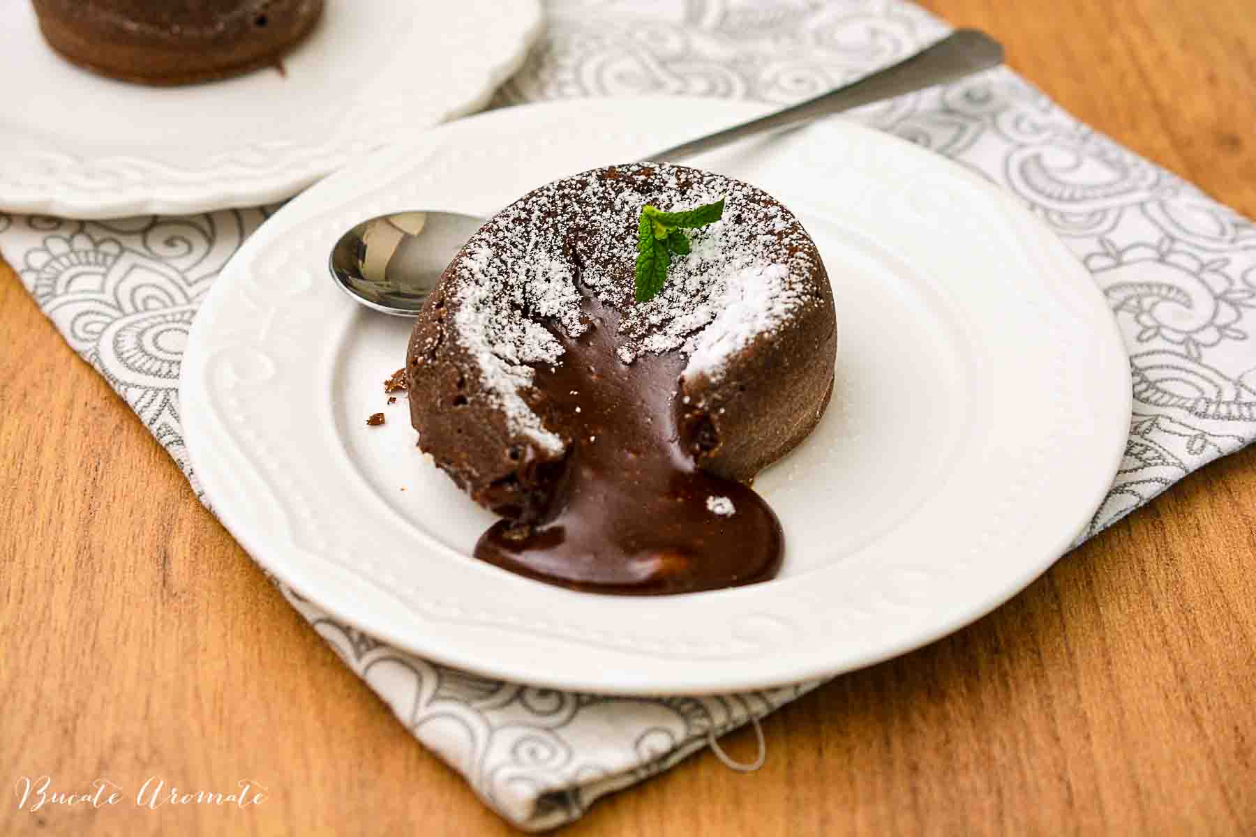Lava cake de ciocolată servit pe farfurie albă, decorat cu frunze de mentă și zahăr pudră
