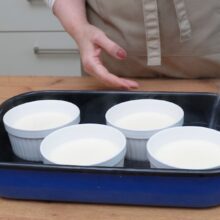 Turnarea apei fierbinți în tava cu formele de crème brûlée pentru coacere la bain-marie.