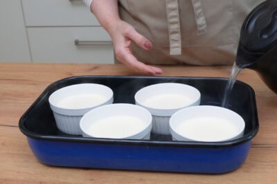 Turnarea apei fierbinți în tava cu formele de crème brûlée pentru coacere la bain-marie.