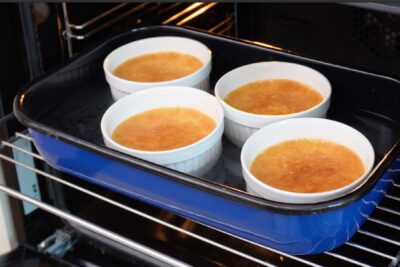 Crème brûlée coaptă în bain-marie, scoasă din cuptor, cu marginile ferme și centrul ușor tremurător.