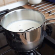 Smântâna pentru frișcă și păstaia de vanilie puse la infuzat într-un vas pe foc.