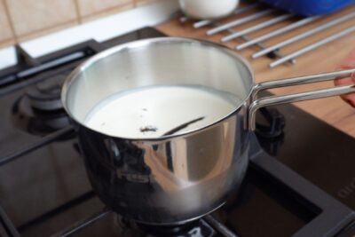 Smântâna pentru frișcă și păstaia de vanilie puse la infuzat într-un vas pe foc.