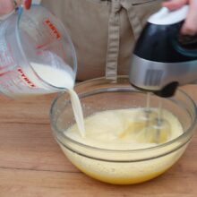 Turnarea treptată a smântânii fierbinți peste amestecul de ouă, în timp ce se mixează.