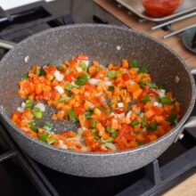 Legume tăiate mărunt (morcov, ardei, ceapă verde) călite într-o tigaie, începutul bazei pentru mâncarea cu cușcuș și pui.