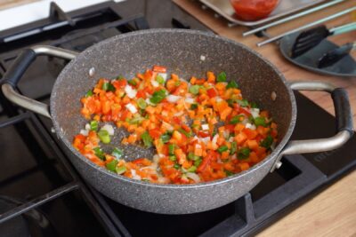 Legume tăiate mărunt (morcov, ardei, ceapă verde) călite într-o tigaie, începutul bazei pentru mâncarea cu cușcuș și pui.