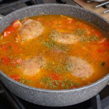 Pulpele de pui acoperite cu apă și condimente, gata să fiarbă în sosul de legume și roșii.