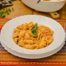 Gros-plan cu paste în sos de roșii și brânză Feta, decorate cu busuioc proaspăt, alături de un pahar cu vin rosé