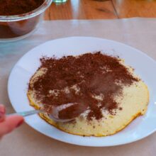 Umplutură de cacao, zahăr și nucă pentru tort de clătite stratificat, presărată pe clătita caldă.