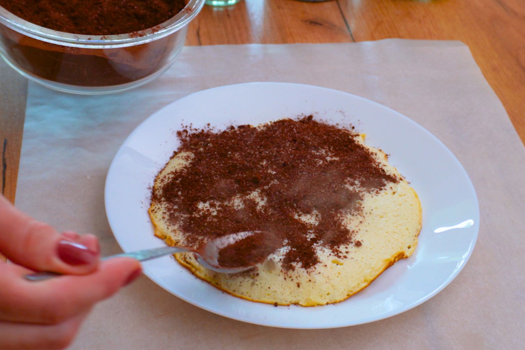 Umplutură de cacao, zahăr și nucă pentru tort de clătite stratificat, presărată pe clătita caldă.