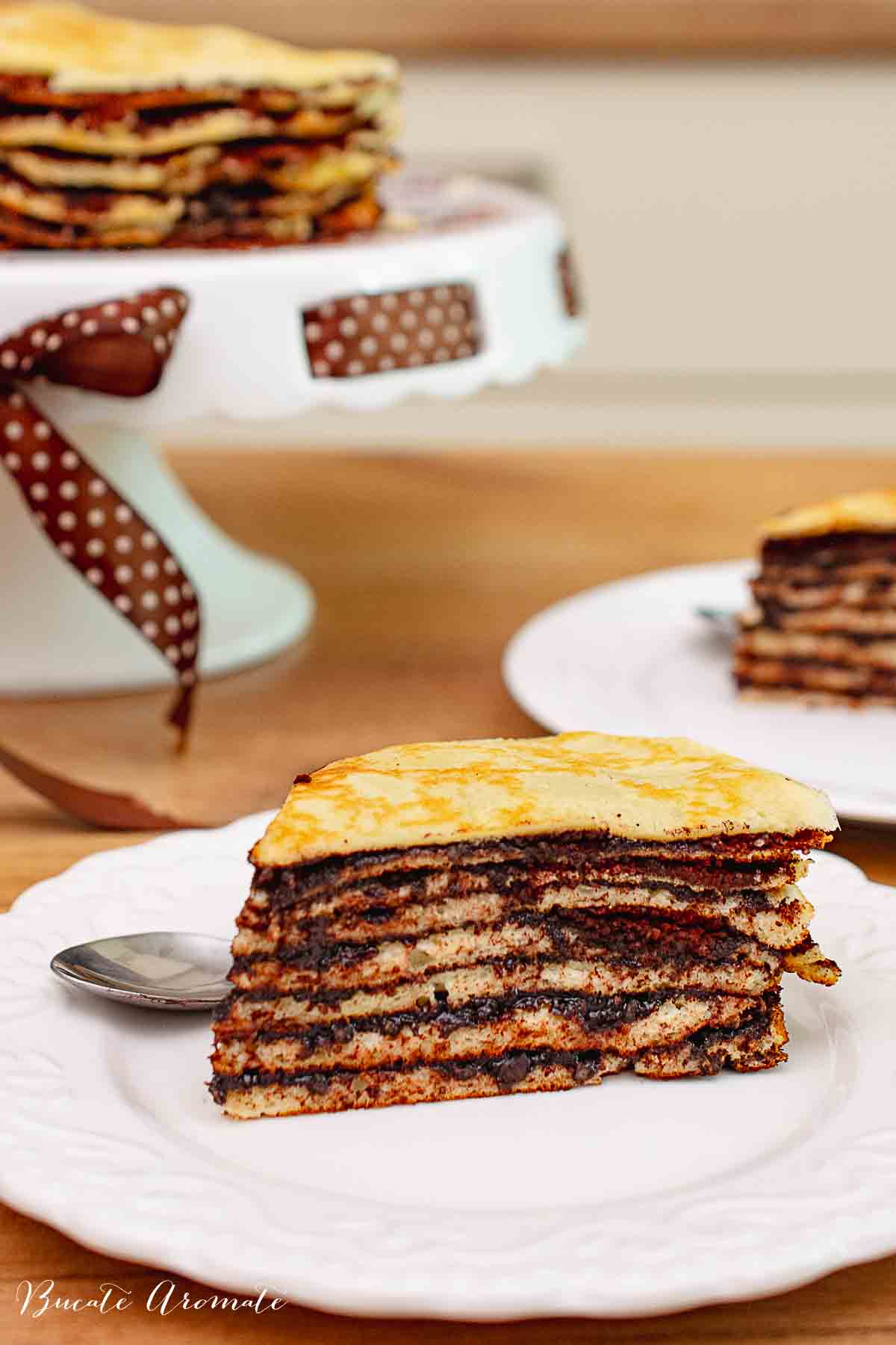 Felie de tort de clătite unguresc cu cacao și nucă, în fața tortului întreg pe suport decorativ