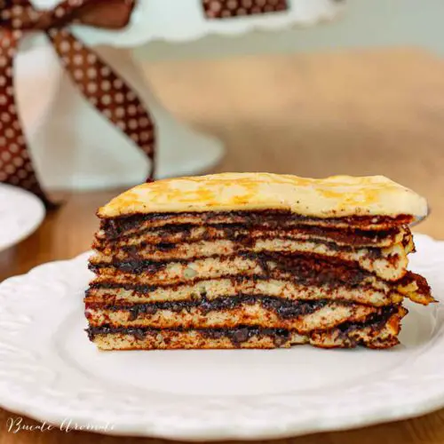 Tort unguresc de clătite în straturi, cu cremă de cacao – felie servită pe farfurie albă